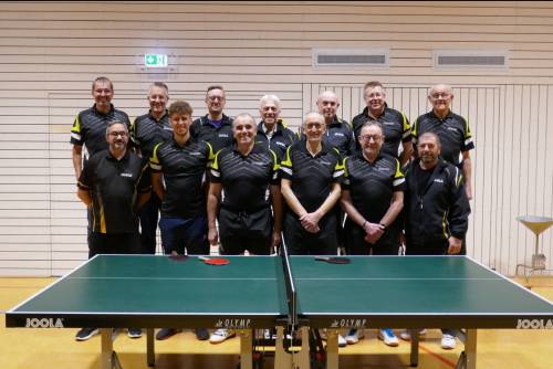 Fünf Männer in schwarzen Shirts stehen neben einem Tischtennistisch und unterhalten sich.